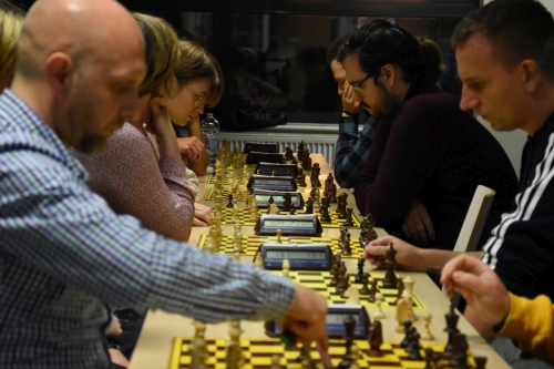 Uczestnicy spotkania, siedzą przy stołach i grają w szachy